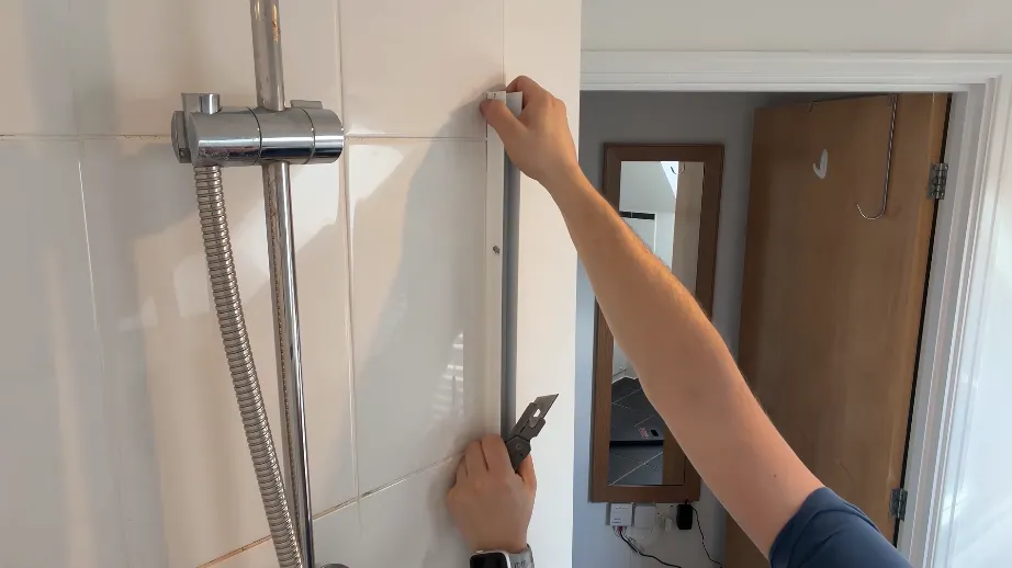 Plumber tightening a shower riser rail fitting on a tiled bathroom wall