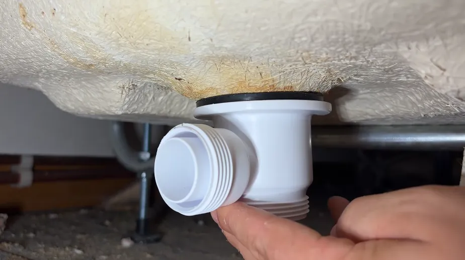 Bathtub waste outlet and trap connection being inspected under a tub